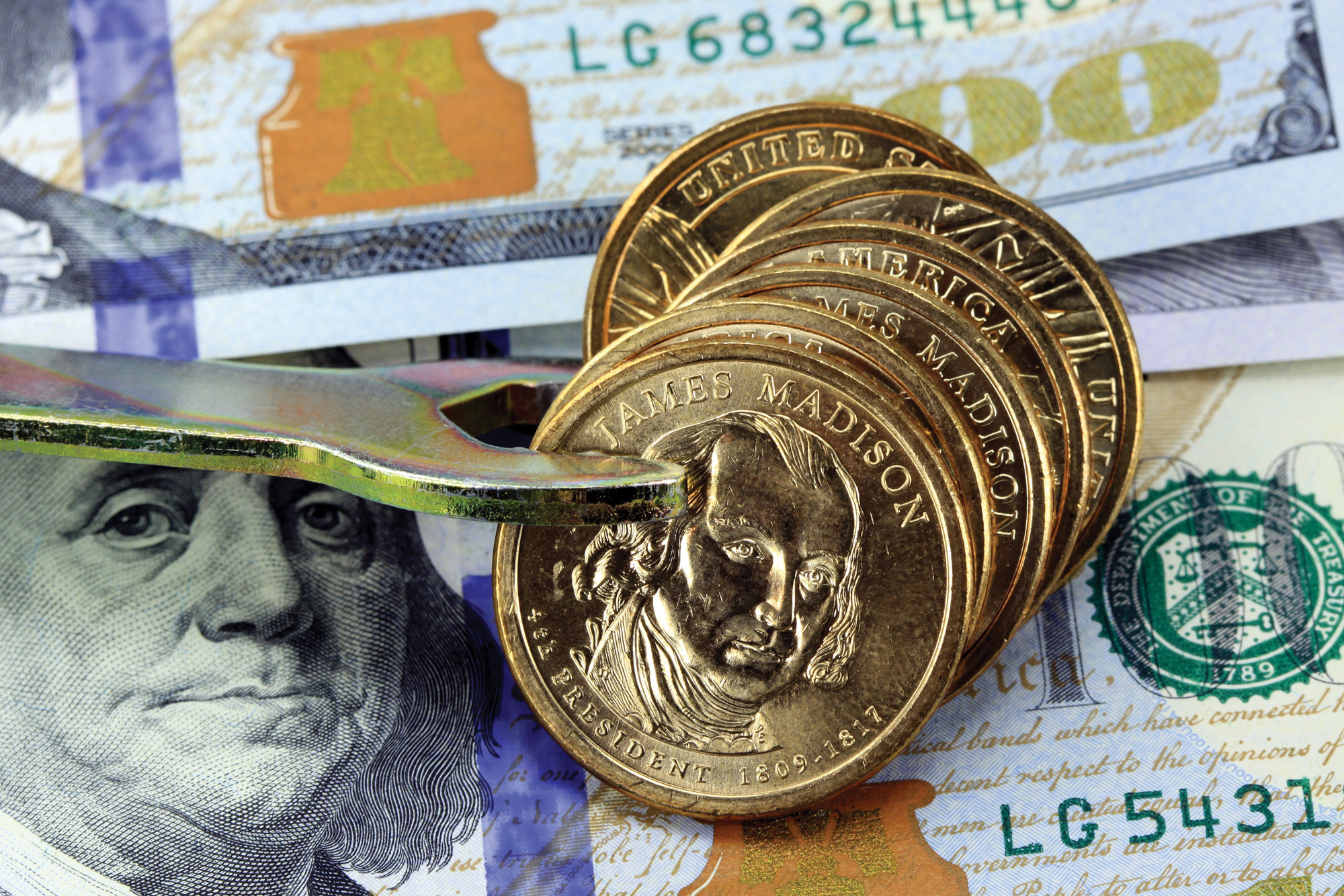 A colorful montage of paper money and gold coins, with a wrench being “applied” to the coins.