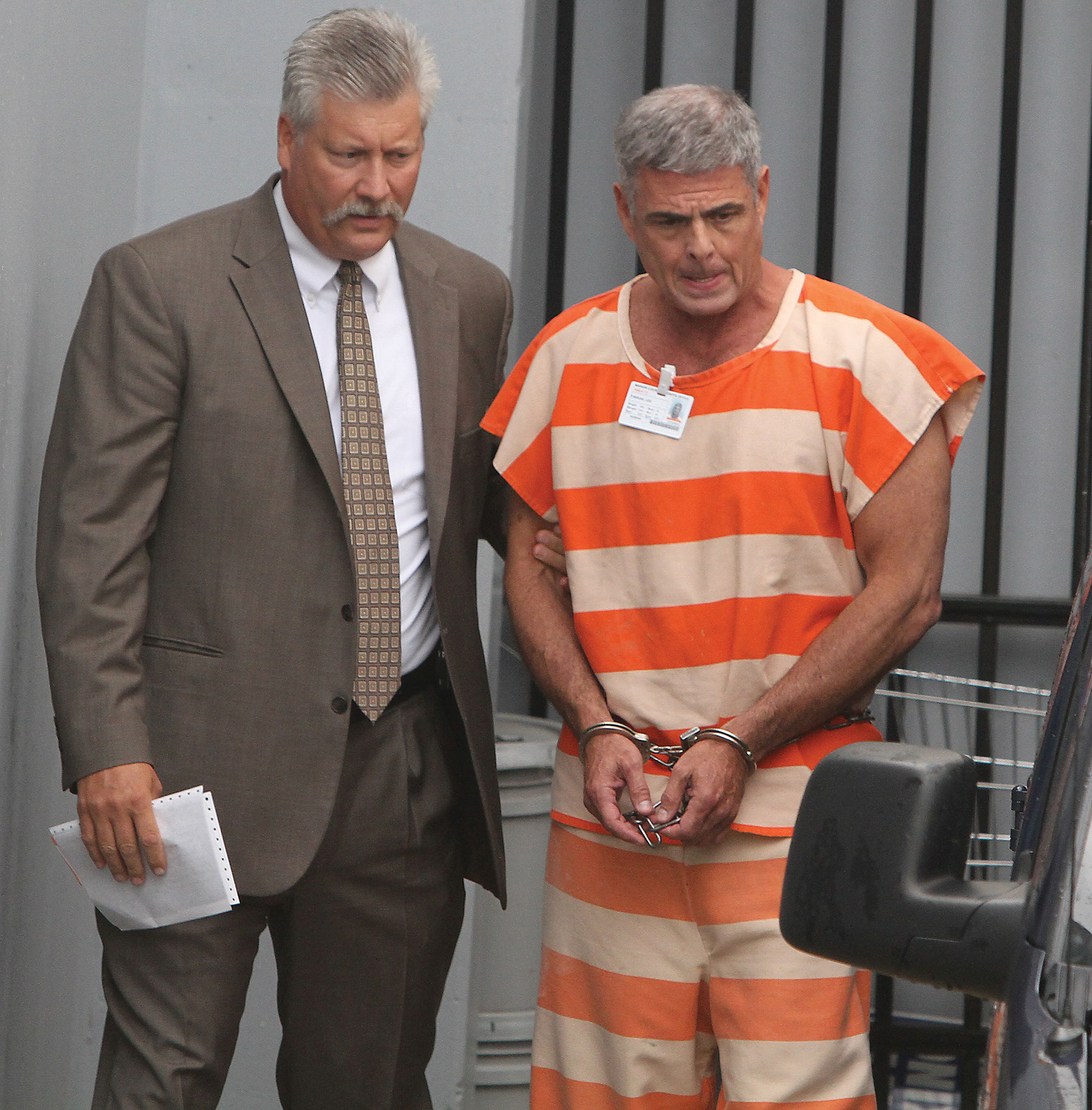 A photo shows a handcuffed Lee Farkas in prison clothes, standing with his lawyer.