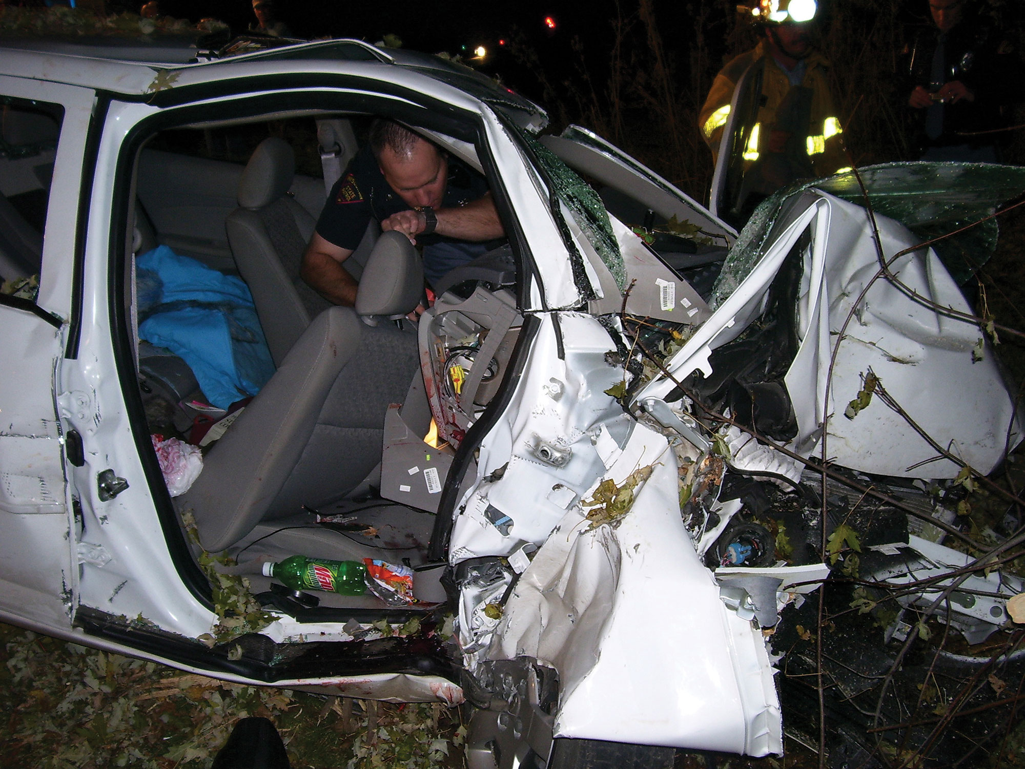 A photo shows a cop investigating a crashed car.