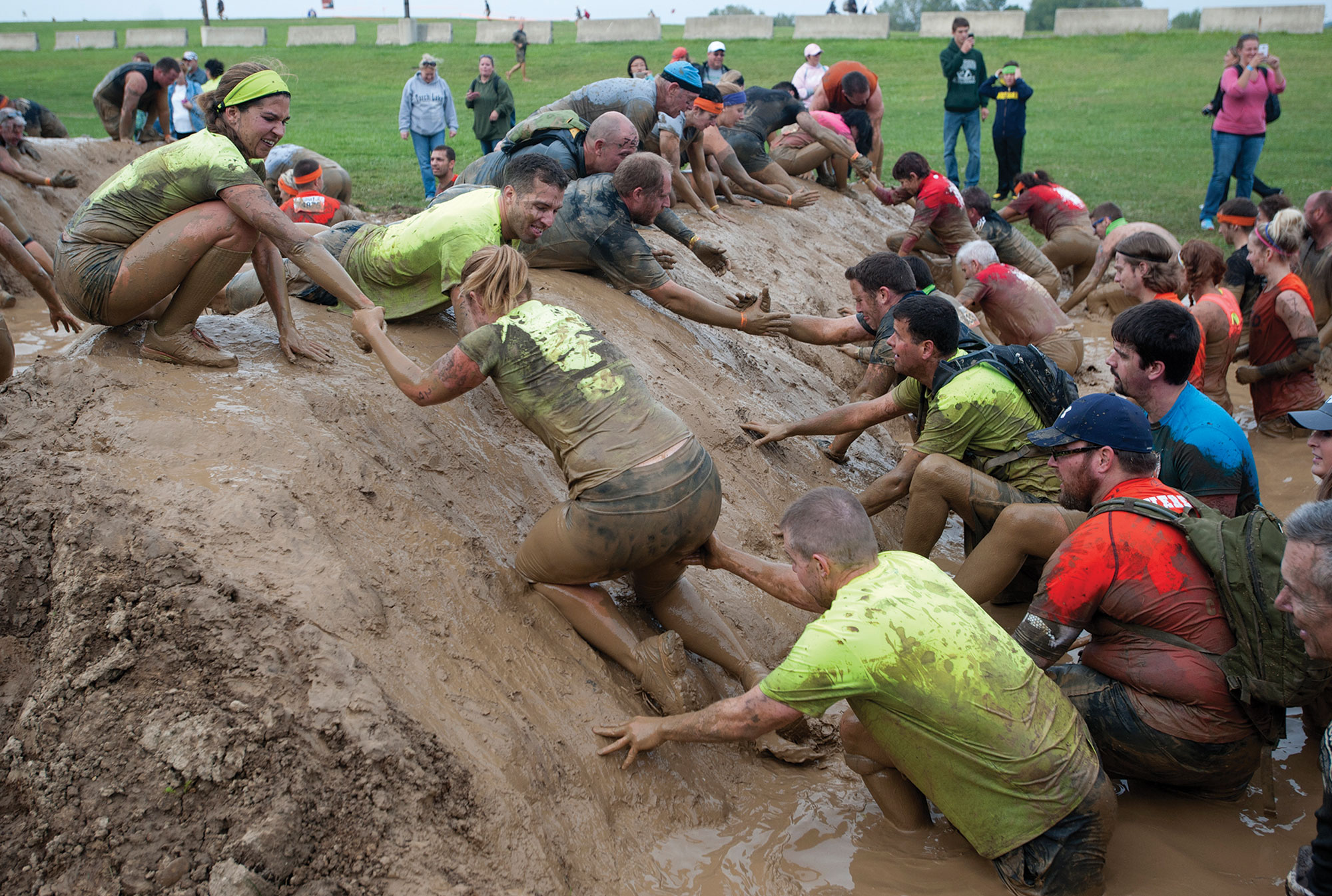 A photo shows people helping other people cross a mud hurdle.