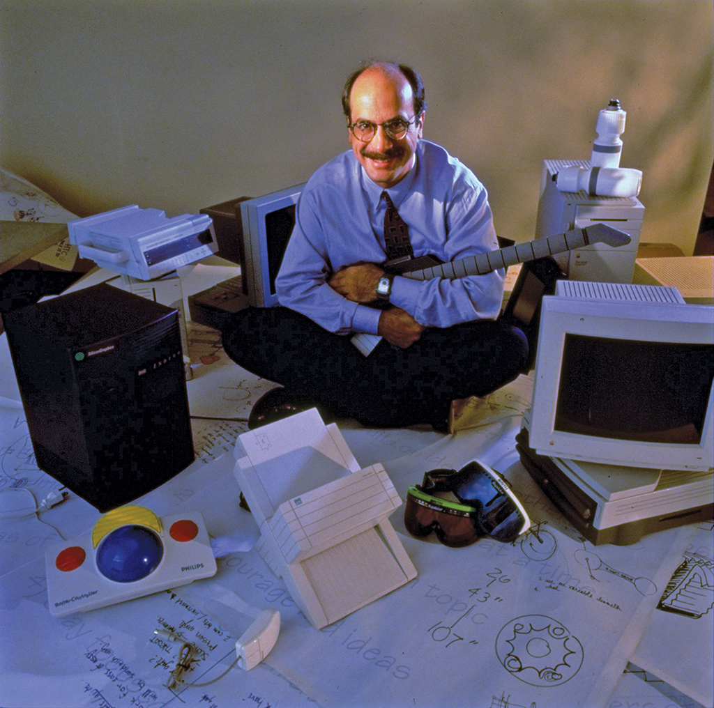 A photo shows a man sitting on the floor with computers and other devices around him.