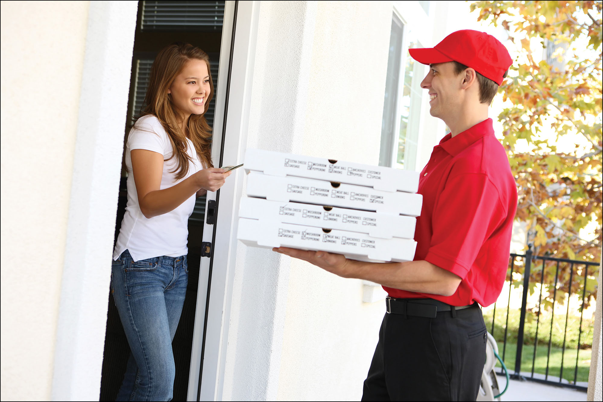 Photo of a pizza delivery man delivering a stack of pizzas to a customer’s home