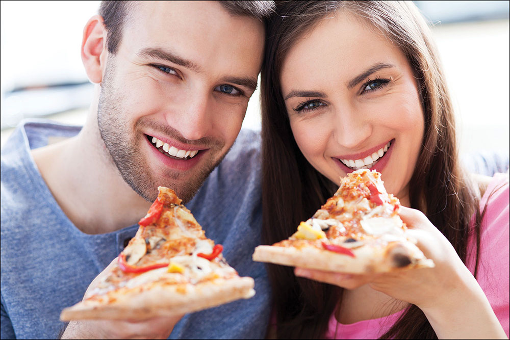 Photo of a smiling couple eating slices of pizza