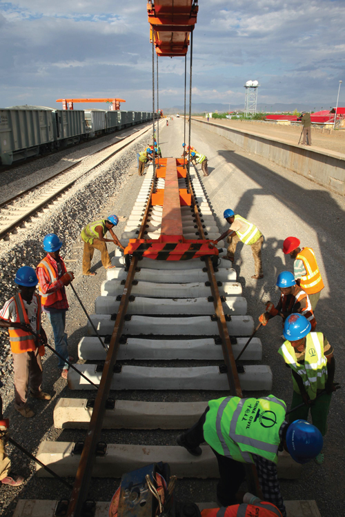 Workers wearing hard hats and reflective vests construct the concrete bed of an electric railway.