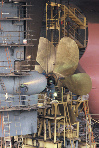 A photo shows workers fitting a propeller to a ship at their assemblage point.