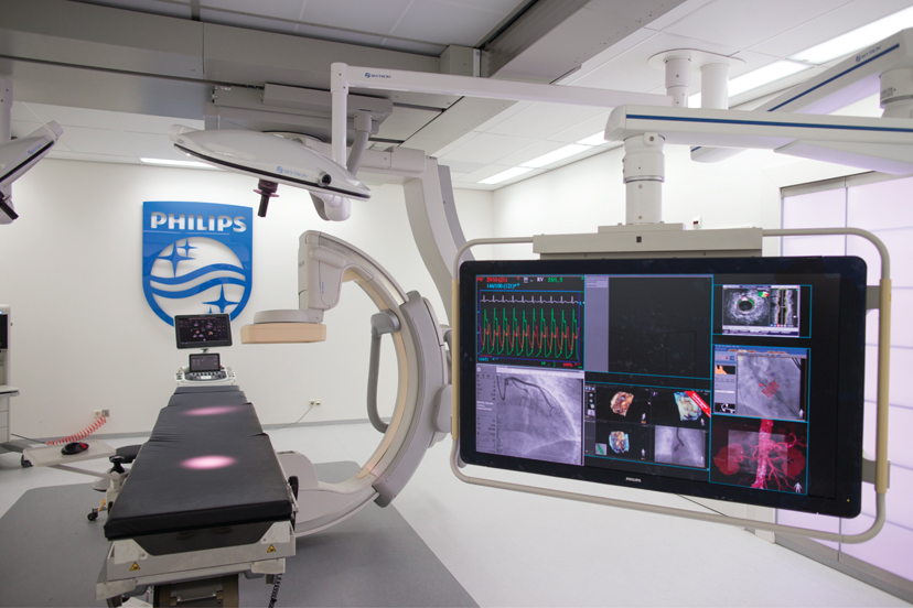 A technologically advanced medical examination room at the Phillips healthcare showroom is well lit, has an examination table, and flat screen technology capable of monitoring patient vitals and viewing x rays.