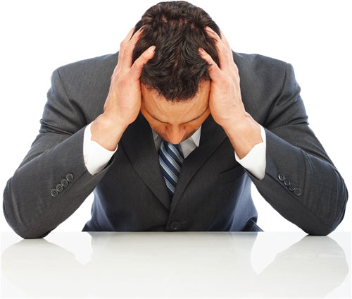 Photo shows a man dressed in a business suit sitting with his head in his hands, suggestive of being in stress.