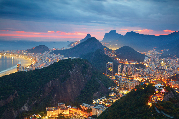 An aerial photo of Rio at night, with the brightly lit beach on one side and the city nestled among the hills and mountains.
