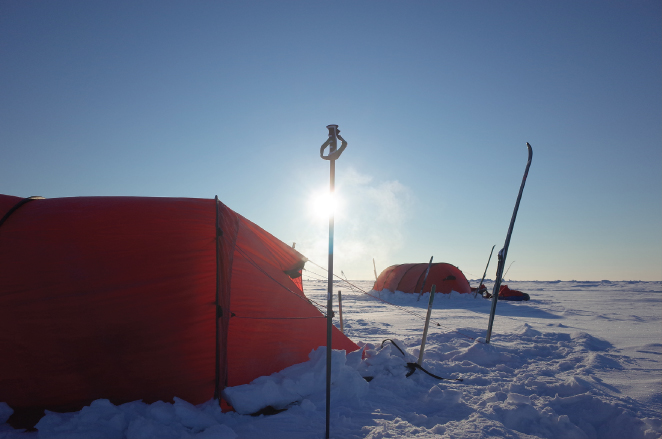 Photograph of two tents tied up to high poles on a vast expanse of ice land.