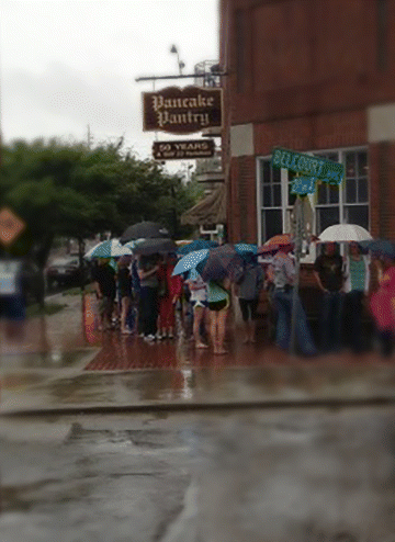 A photograph of one wet, dreary morning outside the Pancake Pantry in Nashville, Tennessee. The customers are carrying their umbrella and waiting in a que for the pancake. This photo perfectly captures the core message of this book and what it means to your business: To be so good at what you do that your customers tell others, creating a steady stream of new customers.