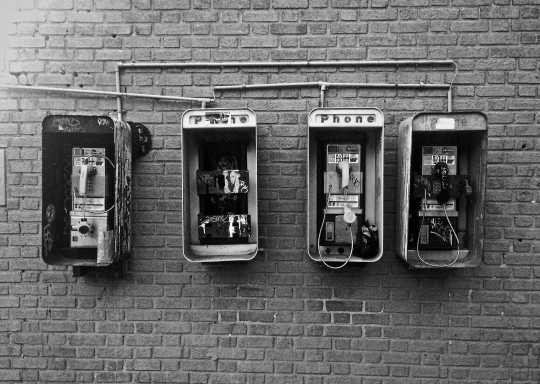 Figure depicting a photograph of four broken payphones installed on a wall.