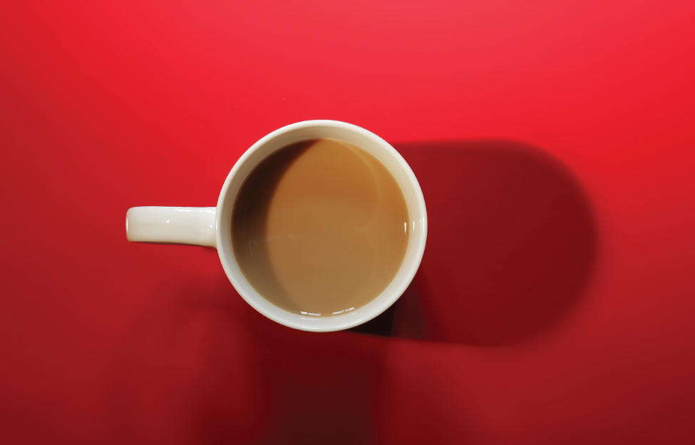 Photograph of coffee in a cup placed on a red surface.
