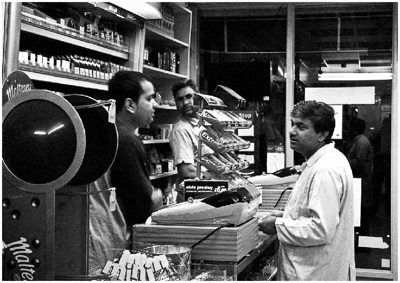 The photograph depicting the view of a shop where two men (shop keepers) are interacting with a customer.