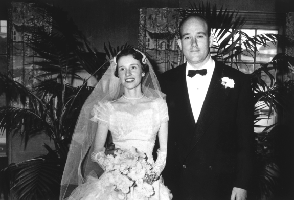 Wedding photograph of Booker and Annis, where Booker is wearing his wedding suite and Annis her wedding gown and holding a bouquet of flowers.