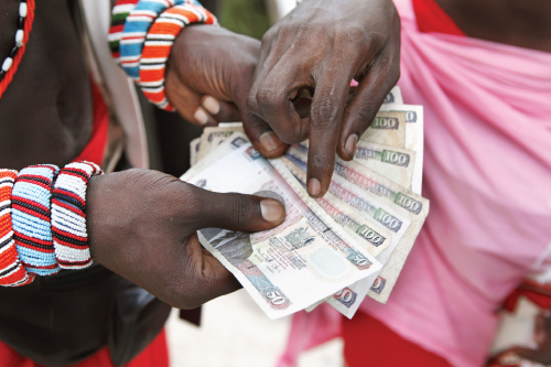 Photo showing a man's hands spread a few currency notes like a fan. Another man's hand is seen touching one of the notes.