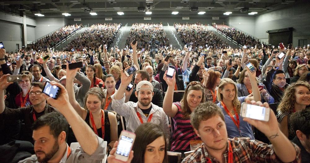 Conference attendees at SXSW Interactive Festival show their phones (photo by Kris Krug).