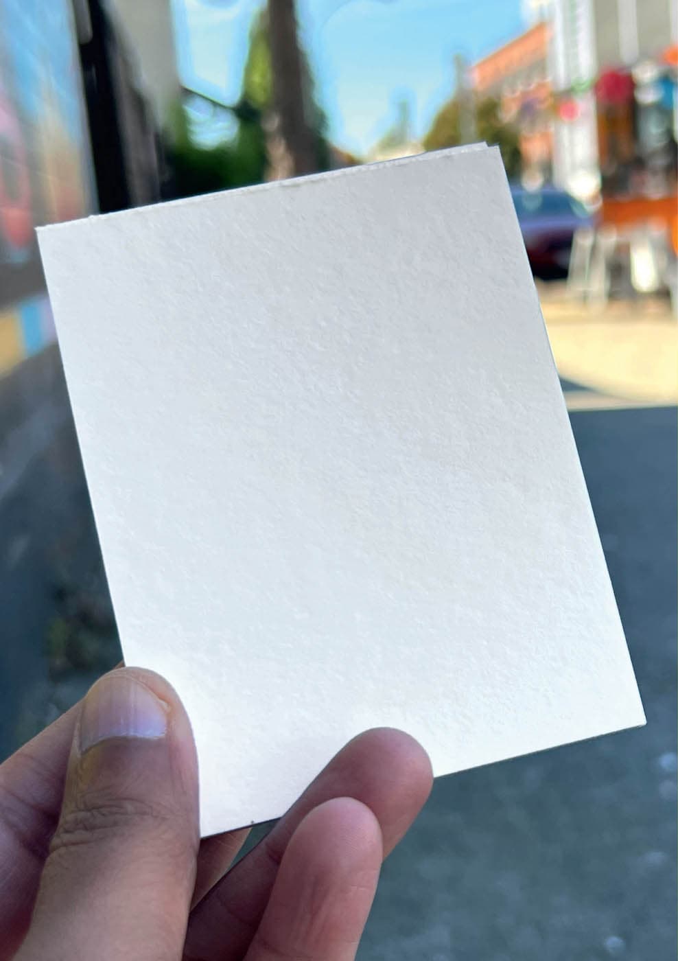 The author holds a blank card against a blurred urban background, symbolizing a blank page or a fresh start.