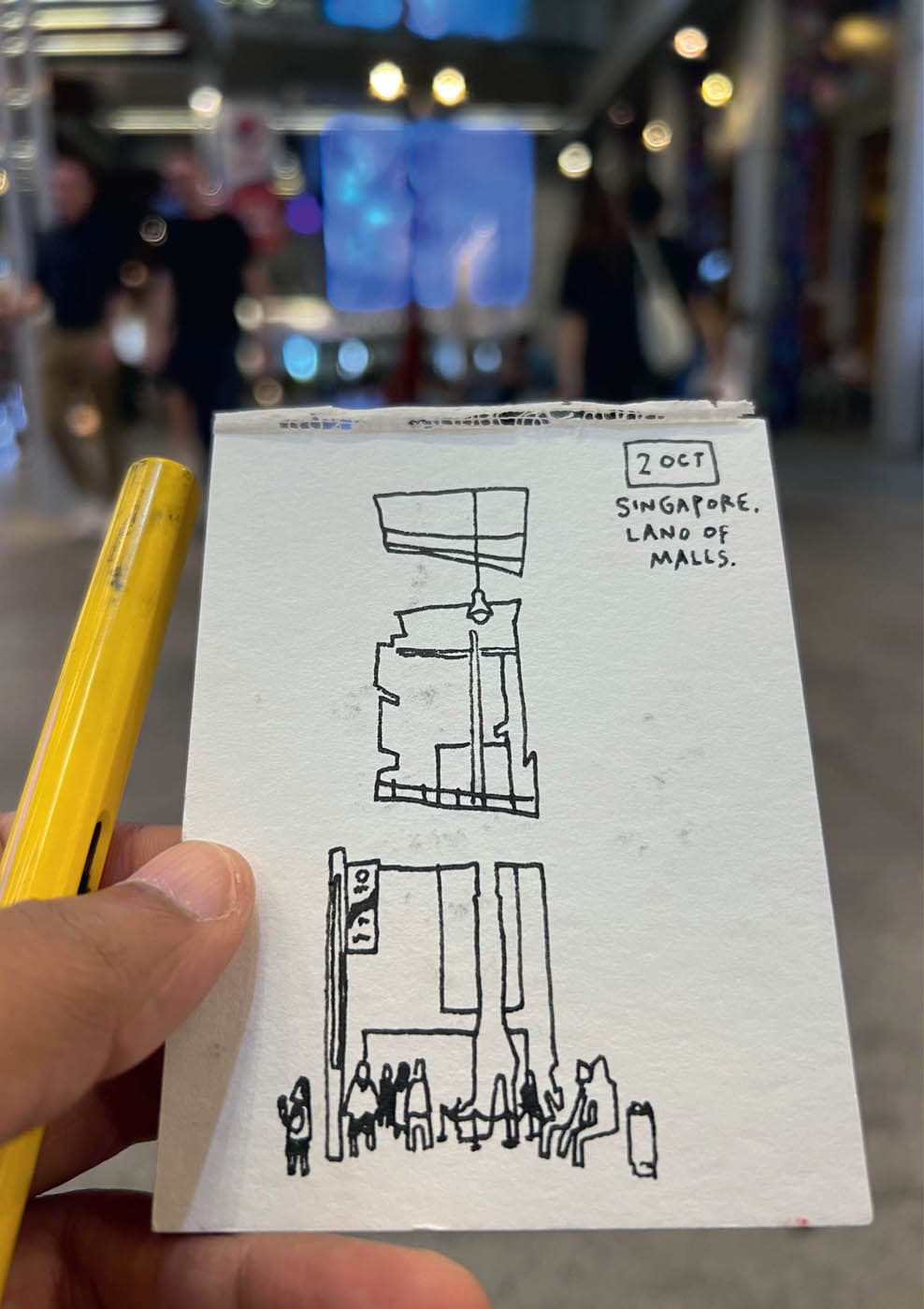 A sketch notebook depicts the interior and exterior of buildings with a street-level crowd scene. This one is from a scene in Singapore.