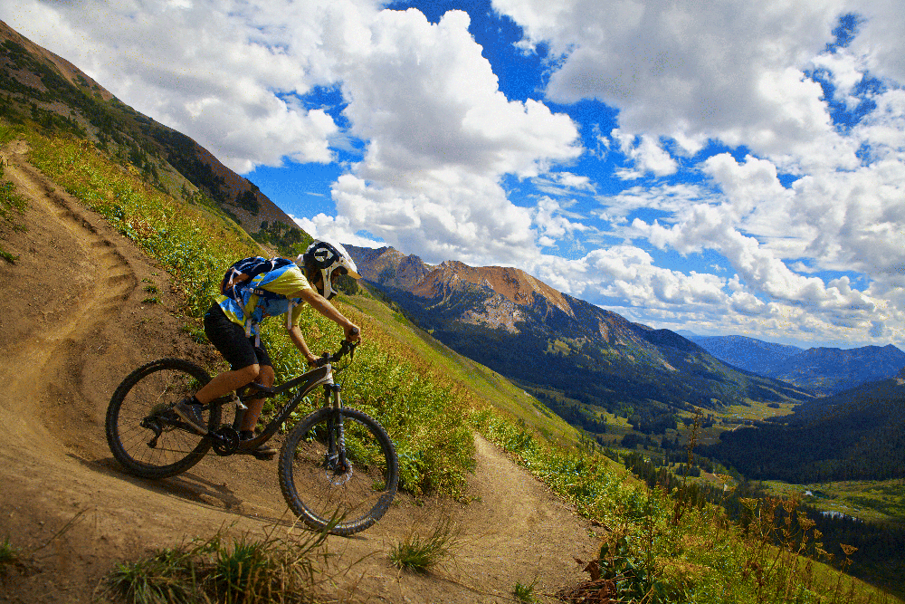 The photograph depicting a person riding on the bicycle in a hilly track under the cloudy sky.