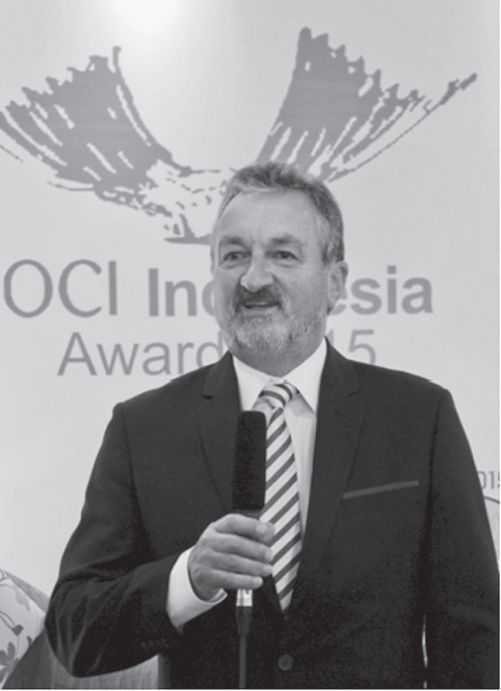 A photograph of a man with a suit holding a mike in his hand doing a presentation and his name is Allan M. Anderson.