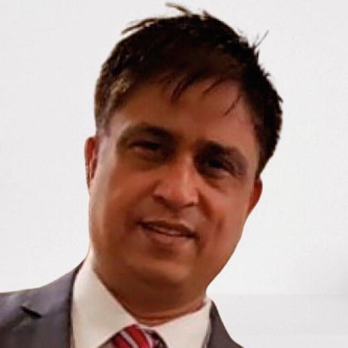 A person in a suit and tie is smiling slightly, looking towards the camera. The background is plain, emphasizing the individual. The image conveys a professional setting.