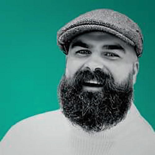 A person wearing a flat cap and a sweater is smiling against a bright green background. The image has a high contrast effect, emphasizing the person's expression.