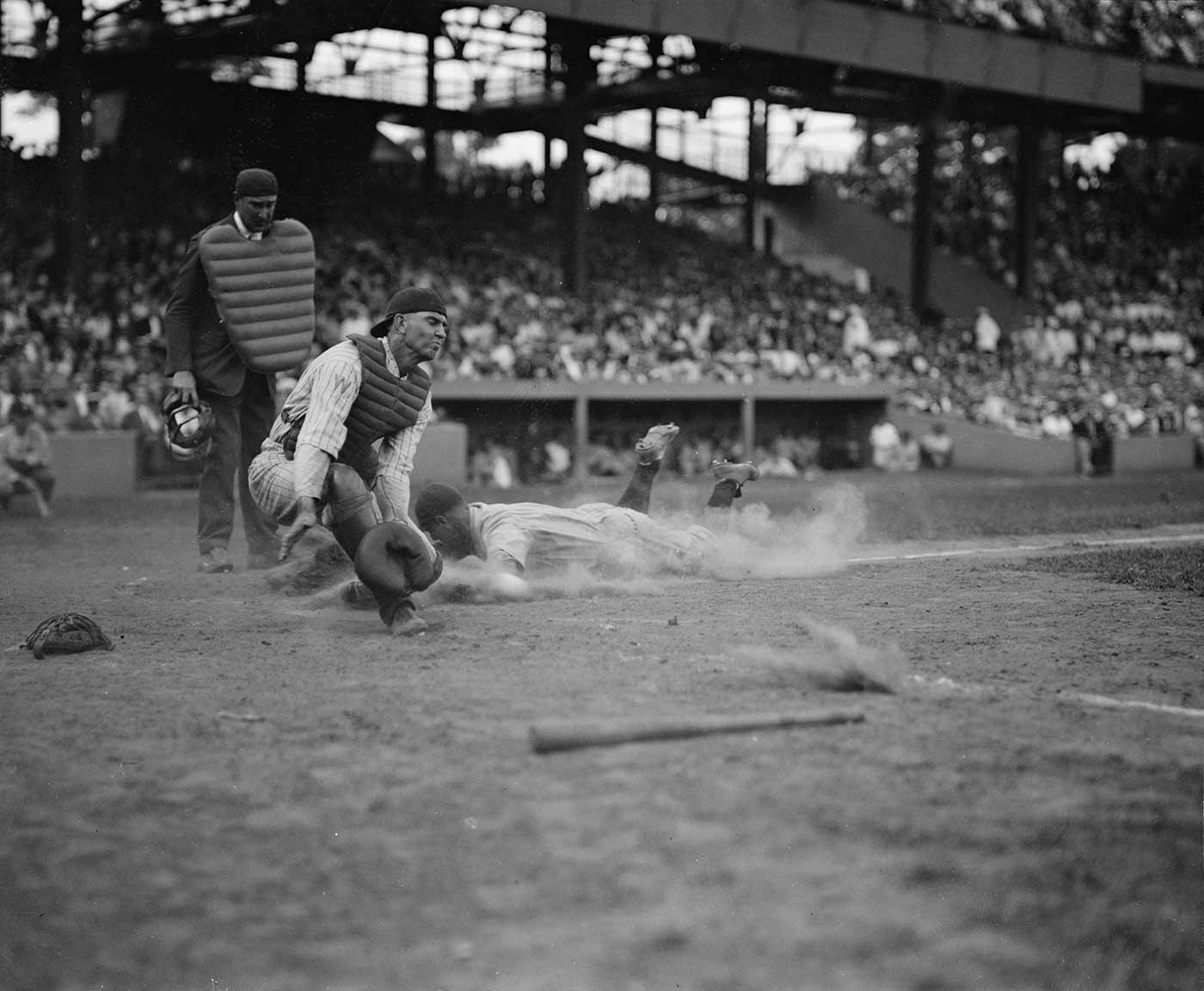 Yankees' Lou Gehrig scores head first in the 4th inning as Joe Harris' throw gets away from catcher Hank Severeid of Senators. Circa 1925.