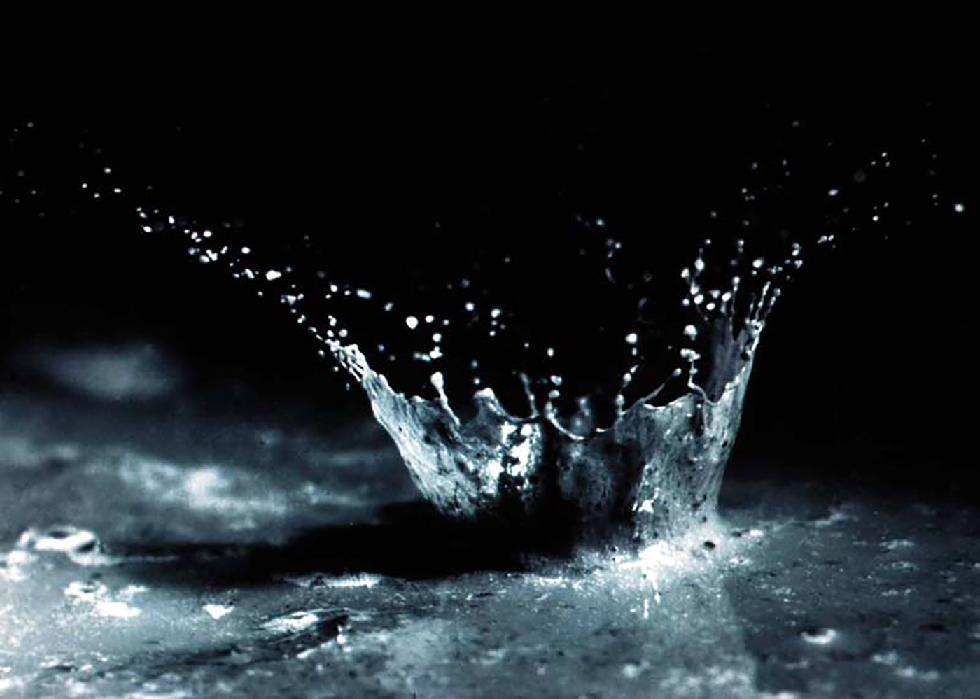 A close-up of water and soil being splashed by the impact of a single raindrop.